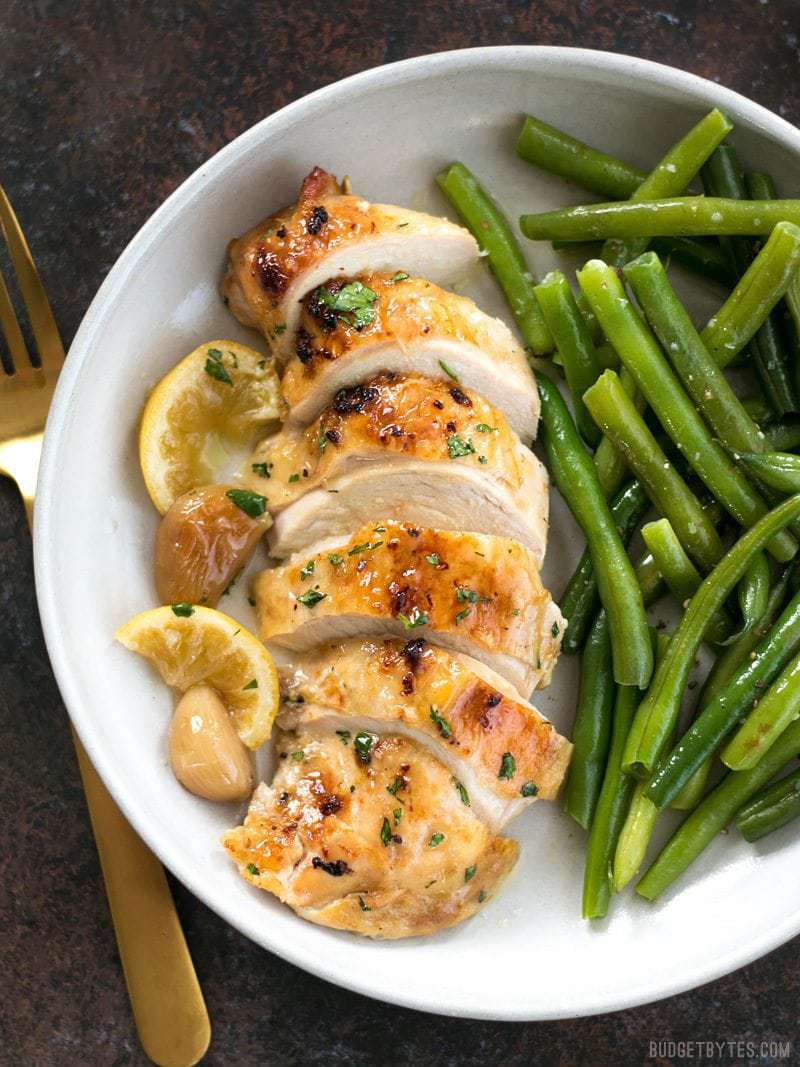 This low and slow cooking method makes this Lemon Garlic Roasted Chicken incredibly tender, juicy, and flavorful! BudgetBytes.com Sliced Lemon Garlic Roasted Chicken on a plate with cooked green beans