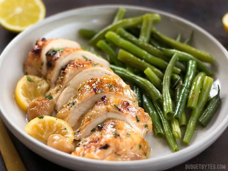 This low and slow cooking method makes this Lemon Garlic Roasted Chicken incredibly tender, juicy, and flavorful! BudgetBytes.com Front view of sliced Lemon Garlic Roasted Chicken on a plate with green beans
