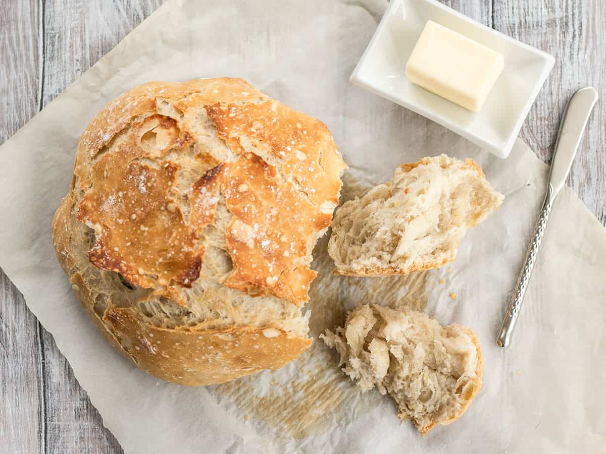 There is no kneading required to make these homemade focaccia rolls that have a crispy exterior and a soft, fluffy interior. Budgetbytes.com Overhead view of a loaf of no-knead bread on parchment with butter on the side.