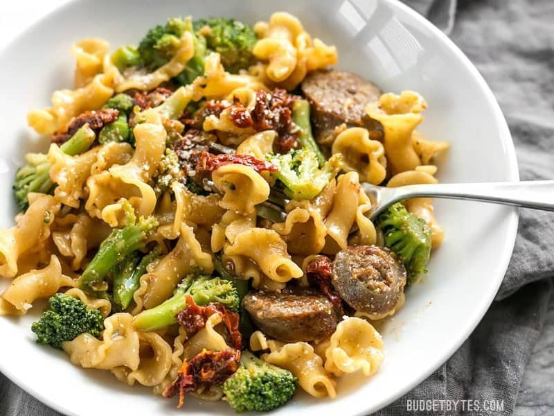 This One Pot Sausage and Sun Dried Tomato Pasta cooks quickly and in one skillet so that no flavor is lost! Make dinner fast, easy, and delicious. BudgetBytes.com Close up of a bowl full of One Pot Sausage and Sun Dried Tomato Pasta with a fork in the side