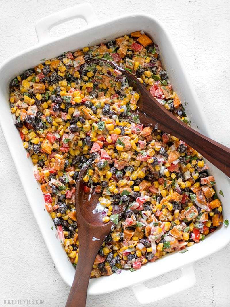 This Roasted Sweet Potato Rainbow Salad combines a medley of vibrant colors and flavors, brought together by a bright and creamy dressing. BudgetBytes.com Roasted Sweet Potato Rainbow Salad in a large serving dish with two wooden serving spoons