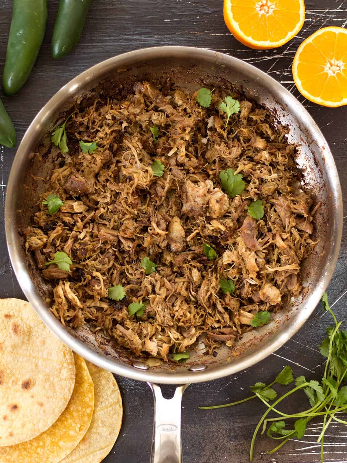Warm spices, fresh orange essence, and a low slow cook time makes this Slow Cooker Carnitas tender, juicy, and full of flavor. Perfect for tacos, burritos and more! Overhead view of finished slow cooker carnitas in a skillet.