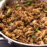 Close up of carnitas in a skillet garnished with cilantro.
