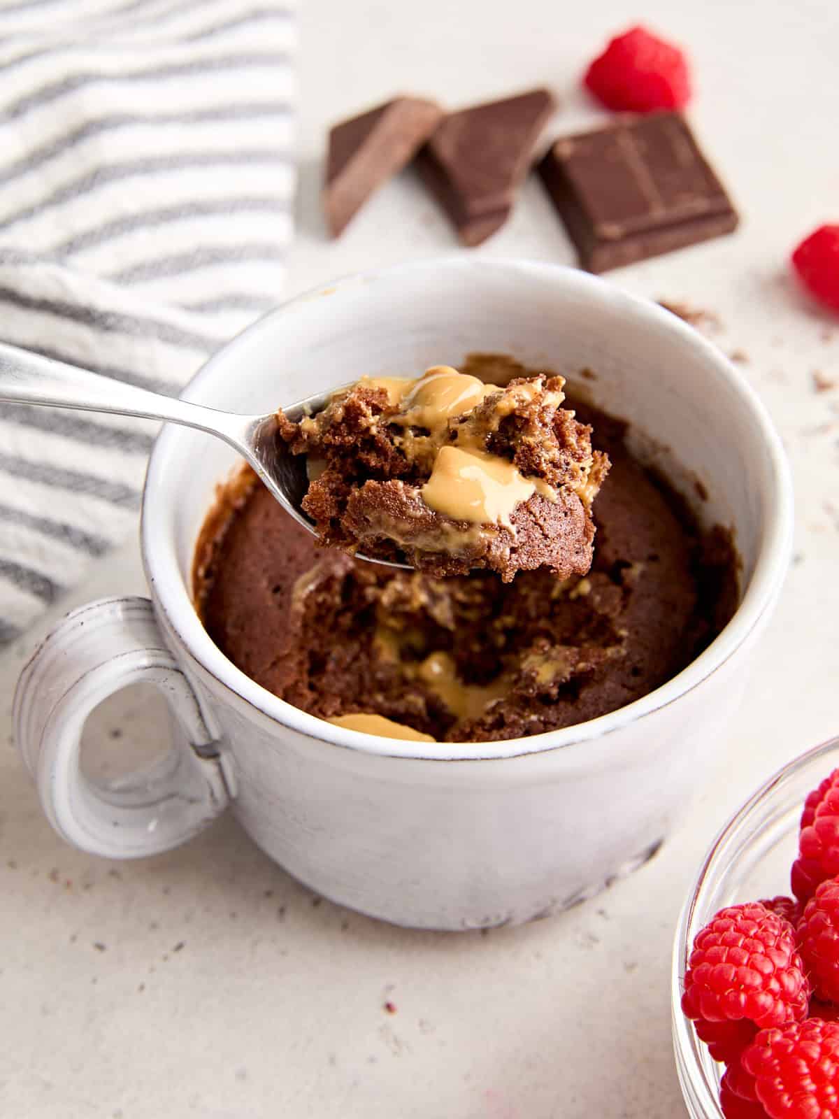 Side view of a chocolate mug cake with a spoon taking some.