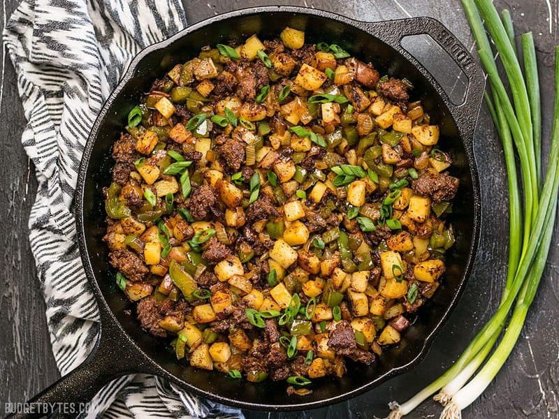 This simple but tasty Chorizo Breakfast Hash is a breakfast classic. Perfect for your lazy weekend brunch, or even "breakfast for dinner". BudgetBytes.com Finished Chorizo Breakfast Hash in a cast iron skillet next to green onion and a striped napkin