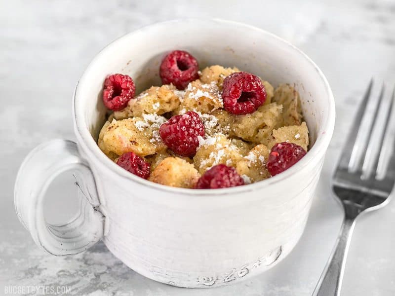 These fast and easy 5-Minute French Toast Mugs are a great single serving breakfast treat plus a way to use leftovers and reduce food waste. BudgetBytes.com Front view of Microwave French Toast Mug topped with raspberries and powdered sugar