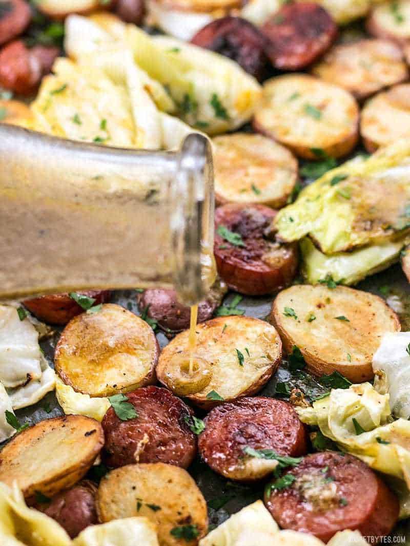 This One Pan Roasted Kielbasa and Cabbage Dinner comes together in minutes and is full of flavor and comfort. An easy weeknight dinner! BudgetBytes.com Vinaigrette being poured onto roasted kielbasa, potatoes, and cabbage