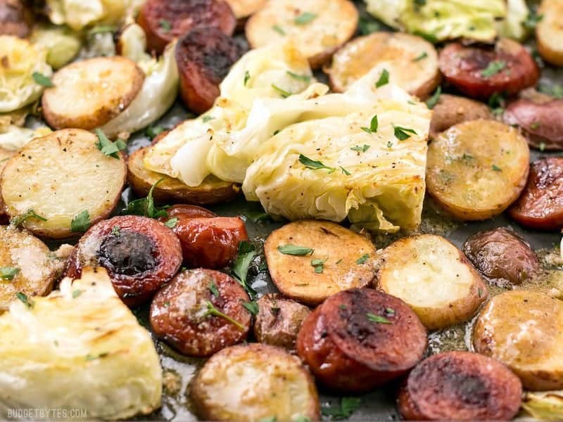This One Pan Roasted Kielbasa and Cabbage Dinner comes together in minutes and is full of flavor and comfort. An easy weeknight dinner! BudgetBytes.com Close up of Roasted Kielbasa and Cabbage Dinner on the baking sheet