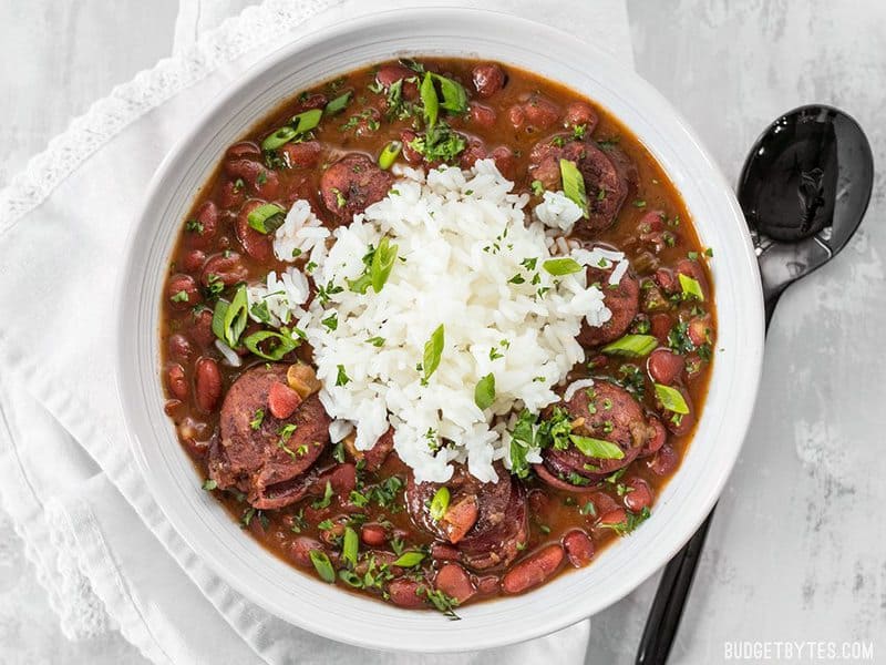 Pressure Cooker Red Beans are a fast, inexpensive, filling, and flavorful staple meal. It's a Louisiana tradition, but FASTER! BudgetBytes.com A big bowl of Pressure Cooker Red Beans topped with white rice, green onion, and parsley