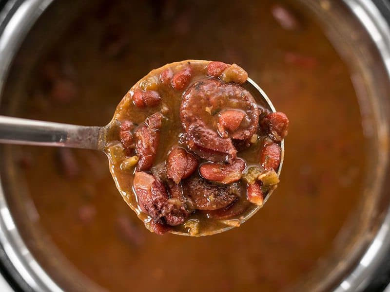 Pressure Cooker Red Beans are a fast, inexpensive, filling, and flavorful staple meal. It's a Louisiana tradition, but FASTER! BudgetBytes.com Close up ladle full of Pressure Cooker Red Beans overhead.