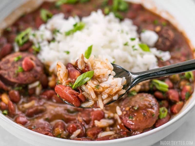 Pressure Cooker Red Beans are a fast, inexpensive, filling, and flavorful staple meal. It's a Louisiana tradition, but FASTER! BudgetBytes.com Close up of a spoonful of Pressure Cooker Red Beans and rice