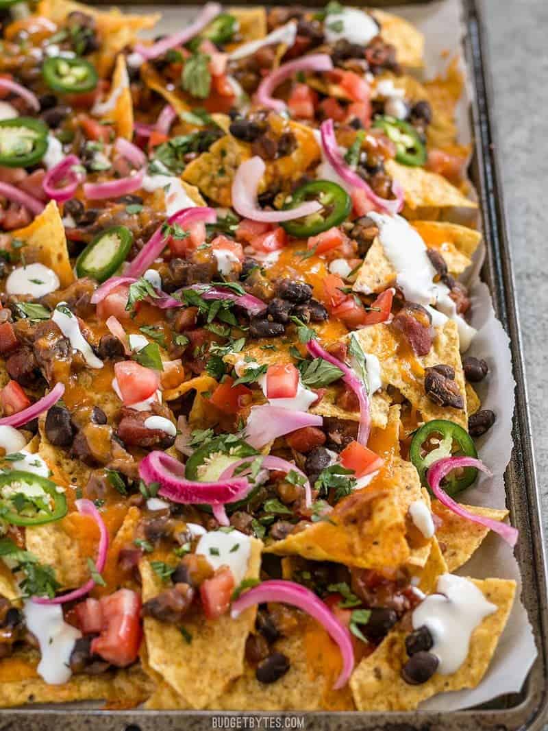 For the perfect Spicy Baked Black Bean Nachos, layer your chips and toppings for the perfect chip-to-topping ratio. BudgetBytes.com Close up of the sheet pan full of Spicy Baked Black Bean Nachos