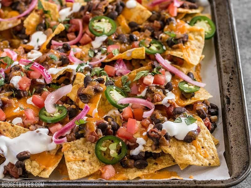 For the perfect Spicy Baked Black Bean Nachos, layer your chips and toppings for the perfect chip-to-topping ratio. BudgetBytes.com Side view of the sheet pan full of Spicy Baked Black Bean Nachos