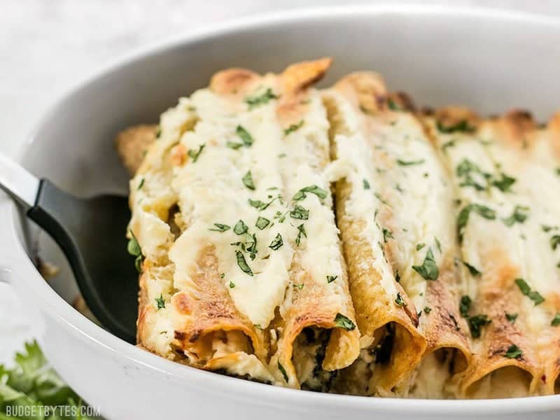 White beans make an inexpensive and fiber filled alternative to chicken in these creamy Spinach White Bean Enchiladas. BudgetBytes.com A spatula lifting Spinach White Bean Enchiladas out of the baking dish