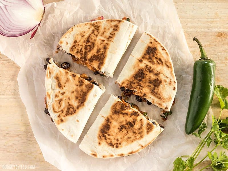 These Ultimate BBQ Chicken Quesadillas are packed with colorful ingredients and deliciously tangy BBQ sauce! #ad BudgetBytes.com A sliced Ultimate BBQ Chicken Quesadilla on a piece of parchment paper