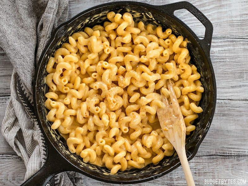 This incredible roux-less mac and cheese is rich, creamy, and only requires seven ingredients. Perfect for last minute weeknight dinners! BudgetBytes.com Overhead shot of a cast iron skillet full of mac and cheese with a wooden pasta fork