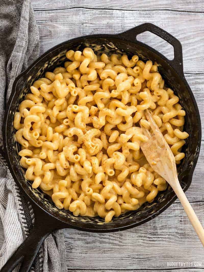 This incredible roux-less mac and cheese is rich, creamy, and only requires seven ingredients. Perfect for last minute weeknight dinners! BudgetBytes.com Finished skillet mac and cheese in a cast iron skillet on a wooden table with a wooden pasta fork
