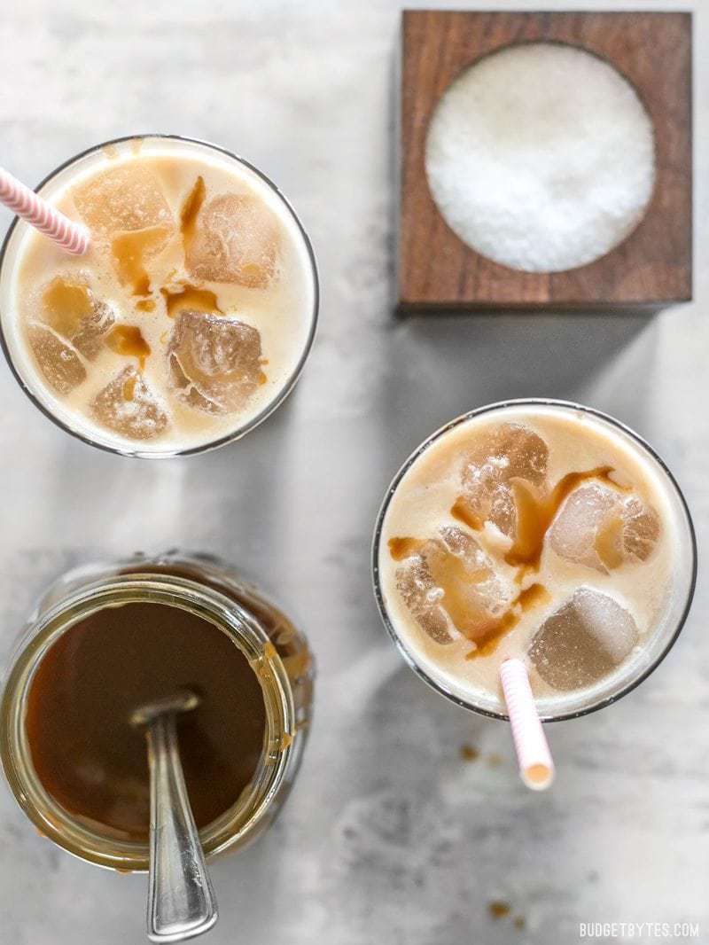 A little fine sea salt helps this Homemade Salted Caramel Iced Coffee stay smooth and taste extra sweet. Make this coffee house favorite at home for less! #ad BudgetBytes.com Two Homemade Salted Caramel Iced Coffees from above with caramel sauce and salt nearby