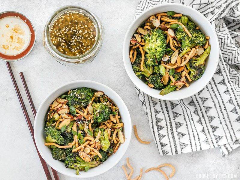 This crunchy, sweet, and salty Roasted Broccoli Salad with Almonds is my favorite way to get my vegetables and goes great with any Asian inspired meal. Budgetbytes.com Two bowls of Roasted Broccoli Salad with Almonds with a jar of simple sesame dressing and a pair of chopsticks