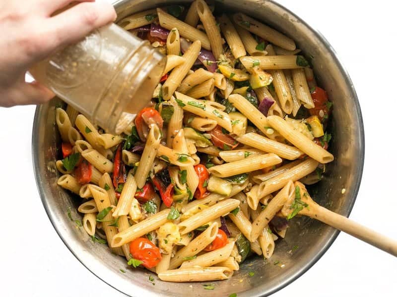 This classic summer Grilled Vegetable Pasta Salad features smoky fire licked vegetables and a homemade creamy balsamic vinaigrette. BudgetBytes.com Balsamic vinaigrette being poured onto Grilled Vegetable Pasta Salad from a mason jar