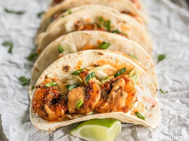 Smoky and spicy shrimp, sweet and tangy slaw, and a zesty garlic lime sauce make these Blackened Shrimp Tacos seriously delicious! Close up front view of Blackened Shrimp Tacos drizzled with garlic lime sauce.
