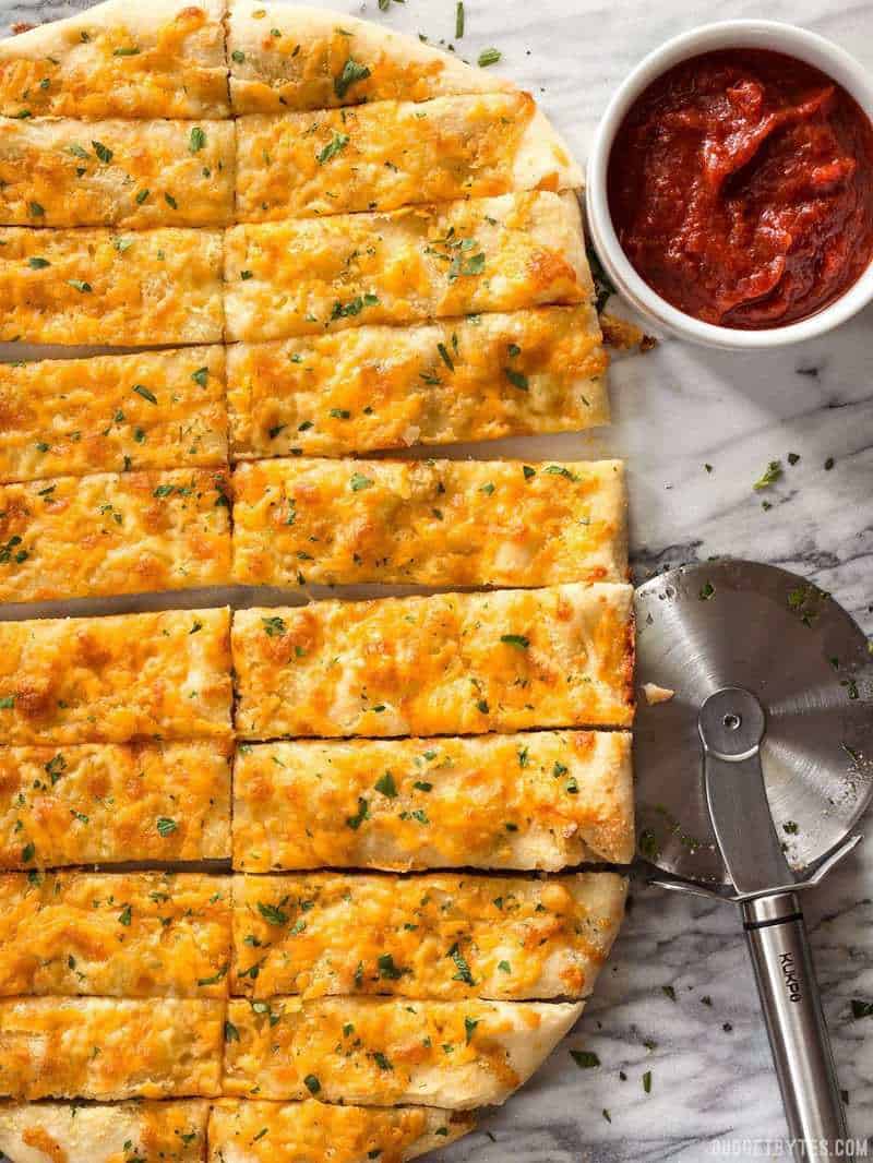 This Homemade Cheesy Garlic Bread is made from scratch with homemade dough, fresh garlic, real butter, and your favorite cheese. Budgetbytes.com Sliced Homemade Cheesy Garlic Bread next to a ramekin full of pizza sauce