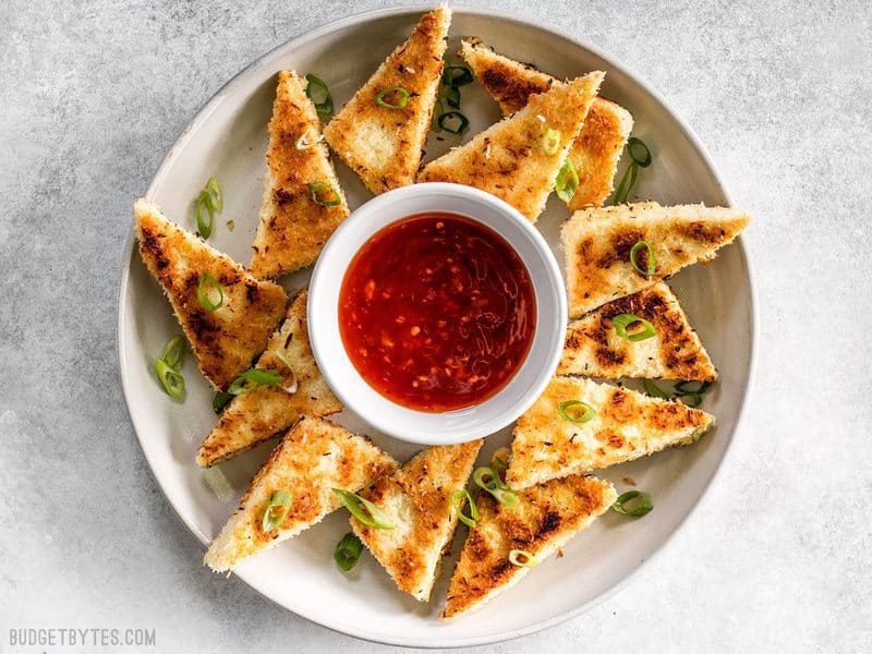These subtly sweet Coconut Crusted Tofu dippers are the perfect vehicle for tangy sweet chili sauce. Serve as a snack or part of your favorite bowl meal. BudgetBytes.com A plate full of Coconut Crusted Tofu dippers with a small bowl of sweet chili sauce in the center