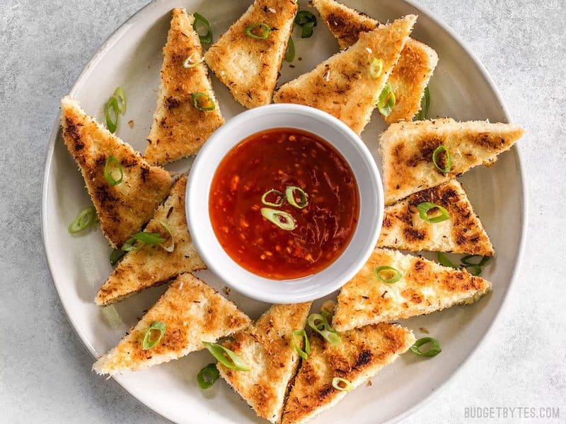 These subtly sweet Coconut Crusted Tofu dippers are the perfect vehicle for tangy sweet chili sauce. Serve as a snack or part of your favorite bowl meal. BudgetBytes.com A plate full of Coconut Crusted Tofu dippers with a bowl of sweet chili sauce in the center