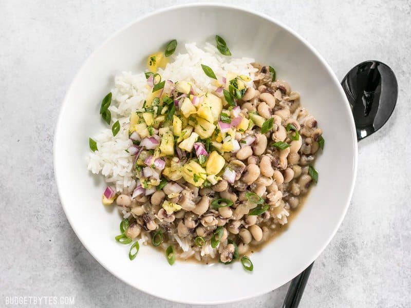 These rich and spicy Coconut Jerk Peas are super simple to make and pair brilliantly with a sweet and vibrant pineapple salsa. BudgetBytes.com A bowl of Coconut Jerk Peas over rice, topped with pineapple salsa
