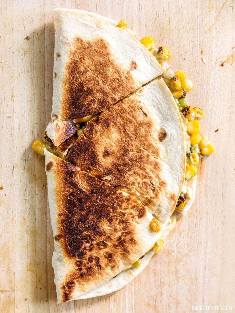 These smoky Roasted Corn Quesadillas are a fast and filling lunch that can be kept in the freezer for fast meals. BudgetBytes.com Sliced Roasted Corn Quesadilla from above, on a cutting board