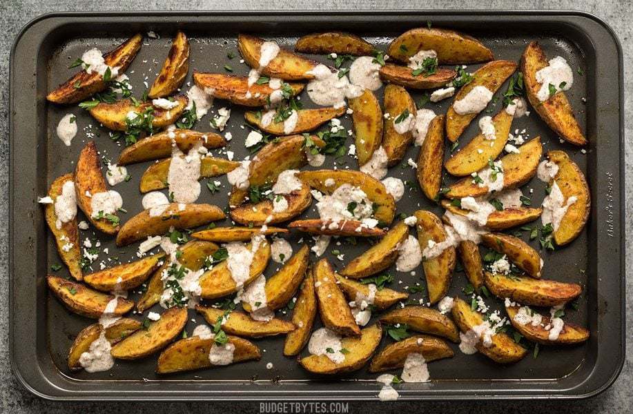 These simple Roasted Potato Wedges are the perfect vehicle for this creamy, garlicky shawarma sauce and crumbled feta. BudgetBytes.com Finished Roasted Potato Wedges with Shawarma Sauce on the baking sheet