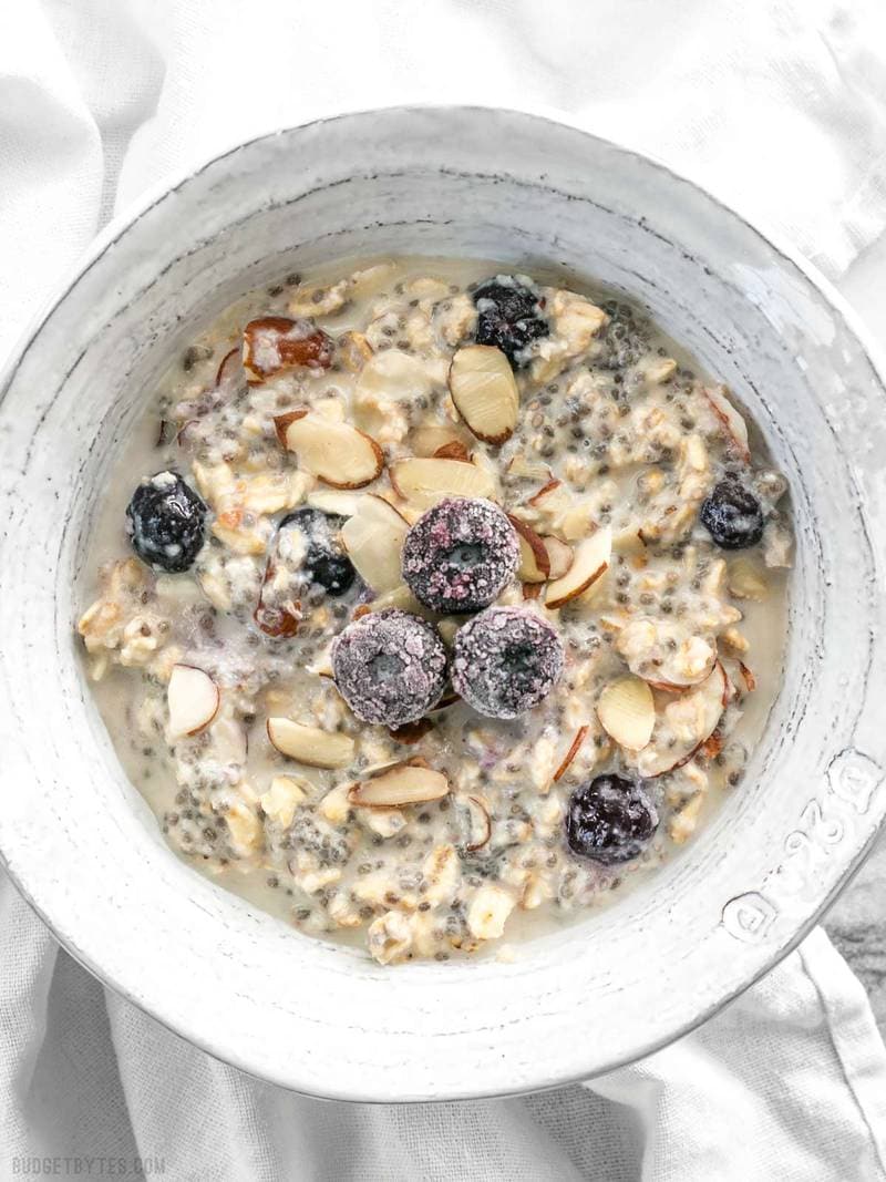 These Blueberry Almond Overnight Oats are naturally sweet without any added sugar, and provide plenty of flavor and texture to keep you happy and full all morning. BudgetBytes.com A bowl of low sugar overnight oats with a few frozen blueberries and almond slices on top for garnish
