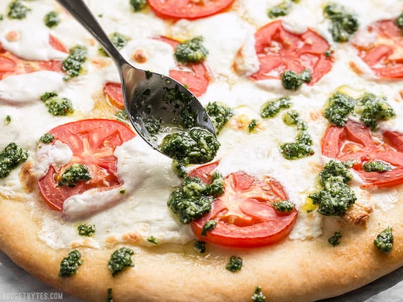 Take your Marghertia pizza up a level with a drizzle of zesty parsley pesto. This white pizza is anything but boring. BudgetBytes.com Parsley pesto being drizzled onto a freshly baked white pizza