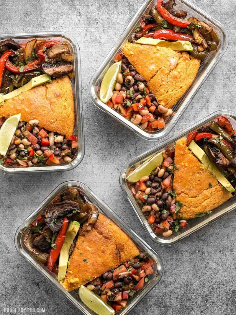 This smoky chipotle portobello fajita meal prep features mixed fajita vegetables, sweet potato cornbread, and cowboy caviar for a filling vegetarian meal! BudgetBytes.com Four glass smoky chipotle portobello fajita meal prep containers scattered on the counter