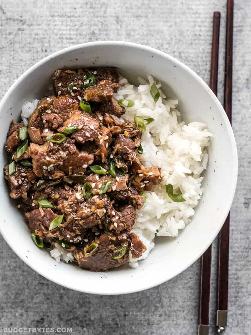 This tender, rich, and flavorful Slow Cooker Sesame Beef is extremely versatile and only requires a few ingredients that can be found at most grocery stores. BudgetBytes.com A bowl of Slow Cooker Sesame Beef served with rice and garnished with green onion and sesame seeds