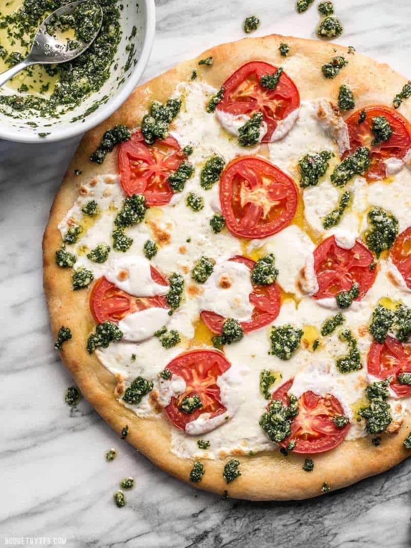 Take your Marghertia pizza up a level with a drizzle of zesty parsley pesto. This white pizza is anything but boring. BudgetBytes.com Bowl of parsley pesto next to the white pizza, some pesto drizzled over pizza