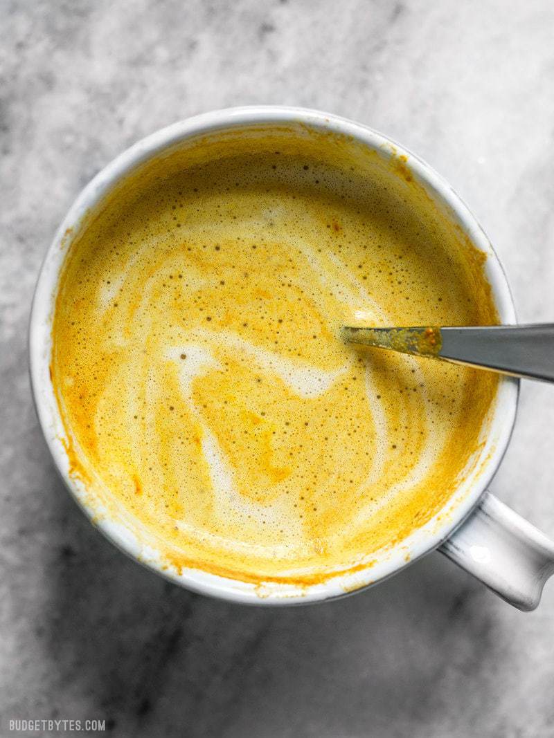 This Golden Chai is full of warm exotic spices, earthy turmeric, and just a hint of natural honey. It's warm, comforting, and perfect for fall! BudgetBytes.com Overhead view of a mug full of Golden Chai with a spoon