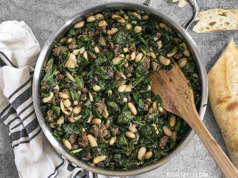 It doesn't get easier than this high protein, high fiber, high FLAVOR Italian Sausage and White Bean Skillet! BudgetBytes.com Finished Italian Sausage and White Bean Skillet on a striped napkin with slices of french bread on the side