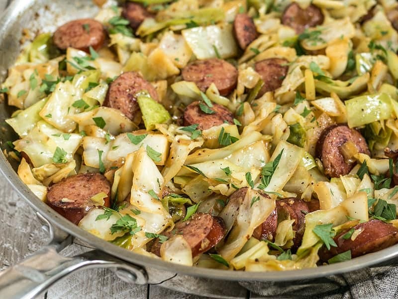This Kielbasa and Cabbage Skillet is a fast and hearty weeknight dinner full of fiber and flavor! Serve with noodles or as is for a lower carb meal. Budgetbytes.com A close up side view of Kielbasa and Cabbage Skillet in the pan.