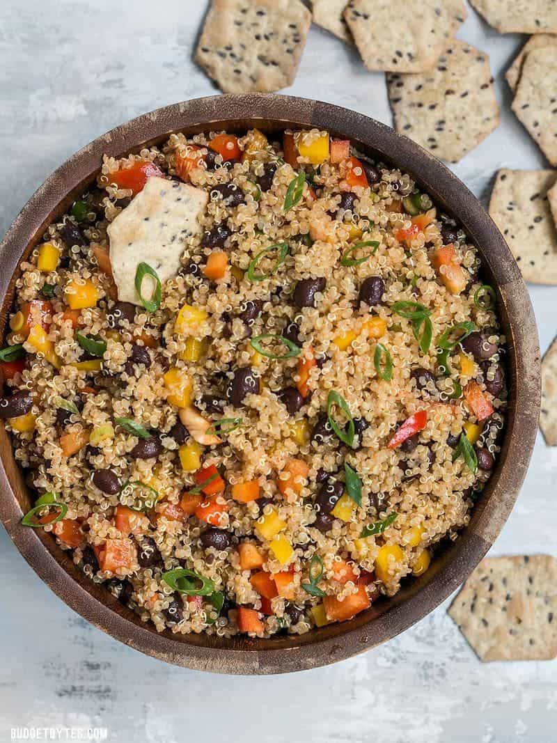 A large wooden bowl full of Smoky Quinoa and Black Bean Salad with crackers all around.