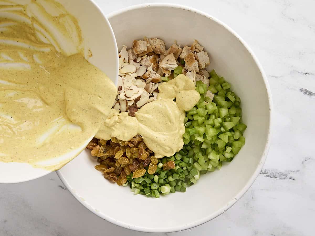 Dressing being poured into the ingredients for chicken curry salad.