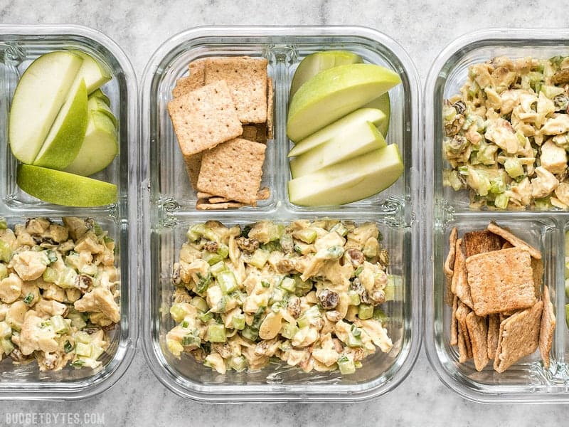 Curry Chicken Salad is paired with crunchy crackers for dipping and a tart apple to cleanse the palate in this simple cold lunch box. BudgetBytes.com Three Curry Chicken Salad meal prep containers in a row