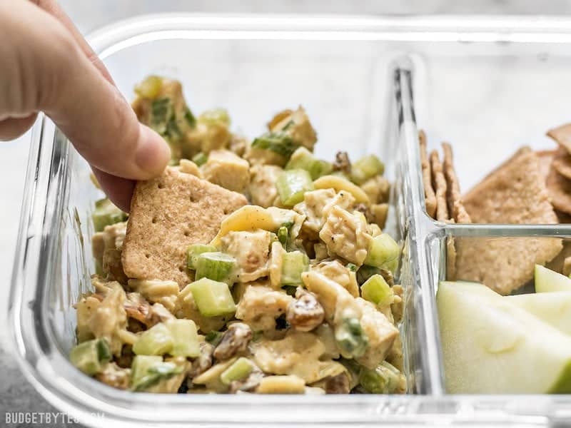 Curry Chicken Salad is paired with crunchy crackers for dipping and a tart apple to cleanse the palate in this simple cold lunch box. BudgetBytes.com A cracker being dipped into Curry Chicken Salad in the meal prep container