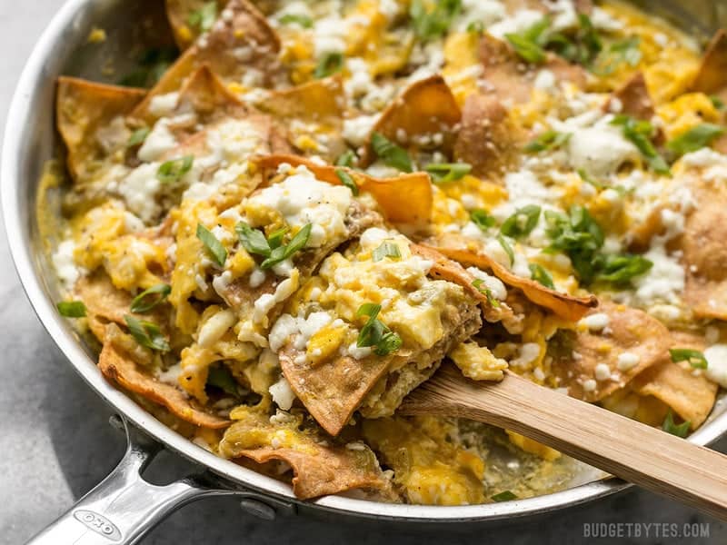 Green Chile Migas is a fast and inexpensive egg dish that is flavorful and filling any time of day, not just for breakfast! BudgetBytes.com Front view of a skillet full of Green Chile Migas being scooped with a wooden spatula.