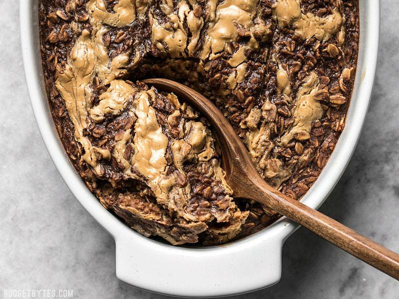 This Peanut Butter Brownie Baked Oatmeal is an indulgent-yet-healthy breakfast with rich chocolatey goodness and just a hint of sweetness. BudgetBytes.com A wooden spoon scooping out Peanut Butter Brownie Baked Oatmeal from the casserole dish
