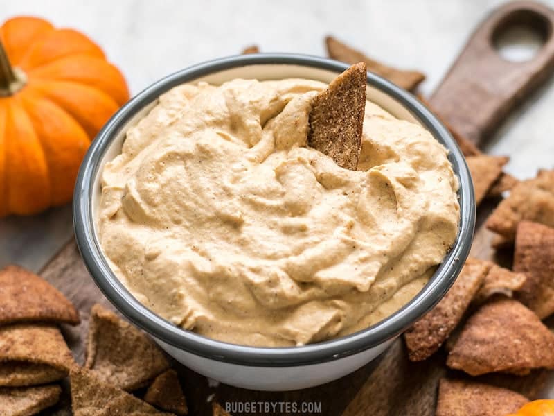 This Pumpkin Cheesecake Mousse is a super light and fluffy no-bake dessert packed with fall spices and just enough sweetness to balance the pumpkin-y flavor. Budgetbytes.com Front view of a Cinnamon Pita Crisp being dipped into a bowl of fluffy Pumpkin Cheesecake Mousse