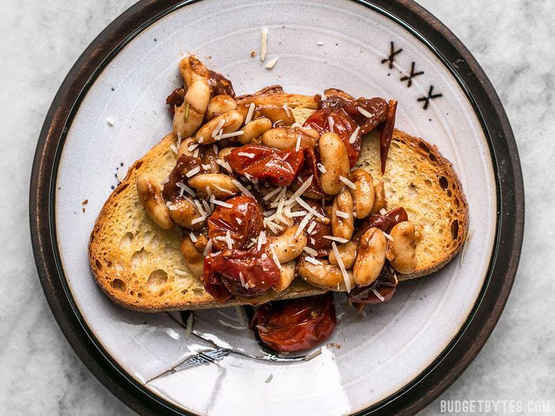 For a quick, flavorful, and light lunch, this Garlic Toast with Balsamic Tomatoes and White Beans hits the spot! BudgetBytes.com Overhead shot of a piece of Garlic Toast with Blistered Tomatoes and White Beans, topped with shredded Parmesan