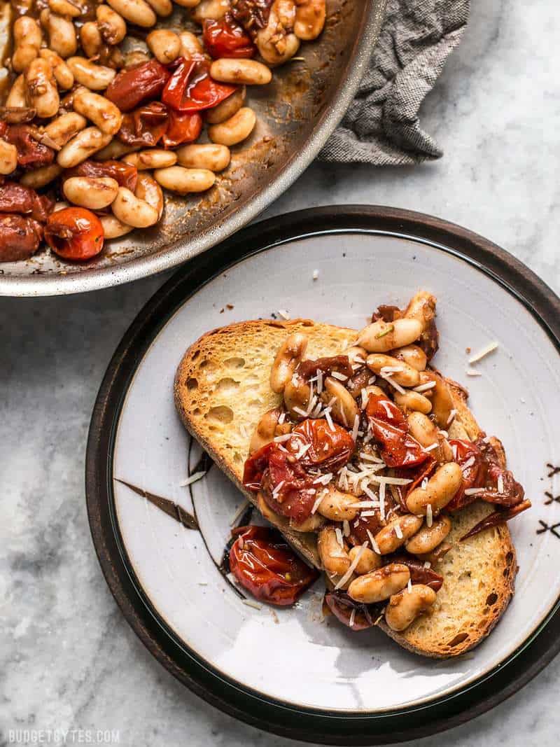 For a quick, flavorful, and light lunch, this Garlic Toast with Balsamic Tomatoes and White Beans hits the spot! BudgetBytes.com A piece of Garlic Toast with Balsamic Tomatoes and White Beans on a plate next to the skillet