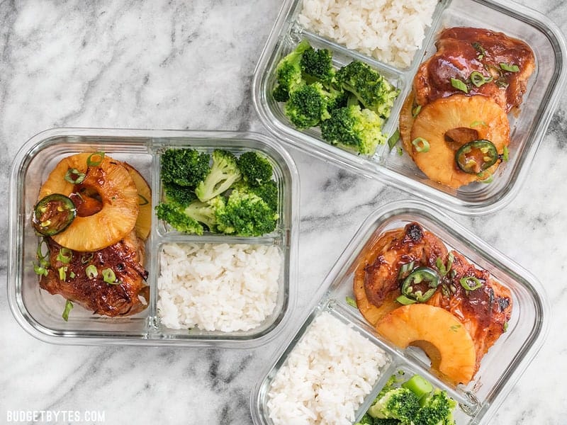 This Pineapple BBQ Chicken Meal Prep includes sweet and tangy chicken, rich and savory coconut rice, and tender broccoli florets. BudgetBytes.com Three Pineapple BBQ Chicken Meal Prep containers scattered