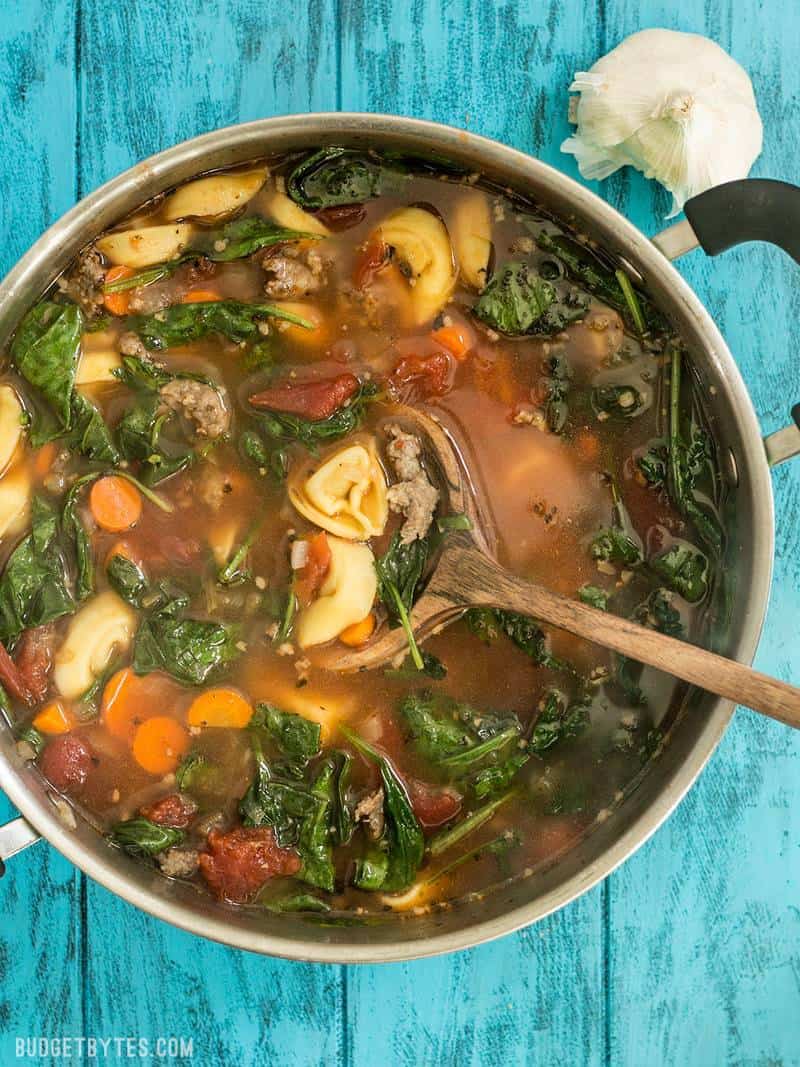 This light but filling vegetable packed Sausage and Tortelloni soup is the perfect lunch for fall. Pair with crusty bread for dipping! BudgetBytes.com Finished pot of Sausage and Tortelloni Soup with a wooden ladle.